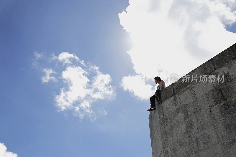 年轻人坐在巨大的混凝土墙上