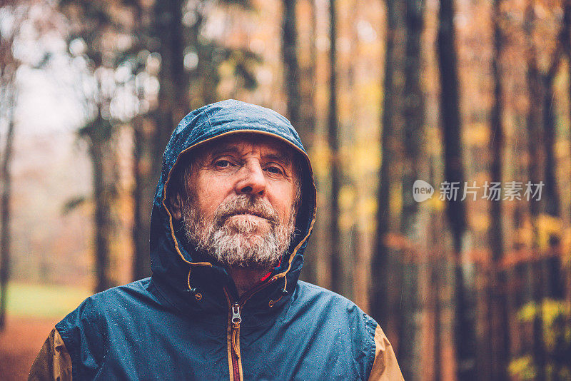 在秋天的山毛榉森林，欧洲，一名高级男子在雨夹克肖像