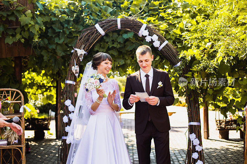 新郎和新娘身穿白色礼服，背景是拱门。婚礼仪式。幸福的家庭