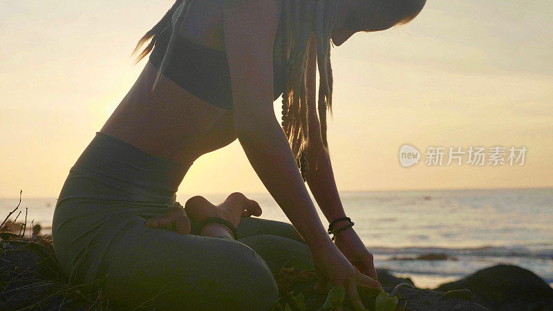 日落时练习剪影瑜伽。一个年轻女人在海滩上做瑜伽运动