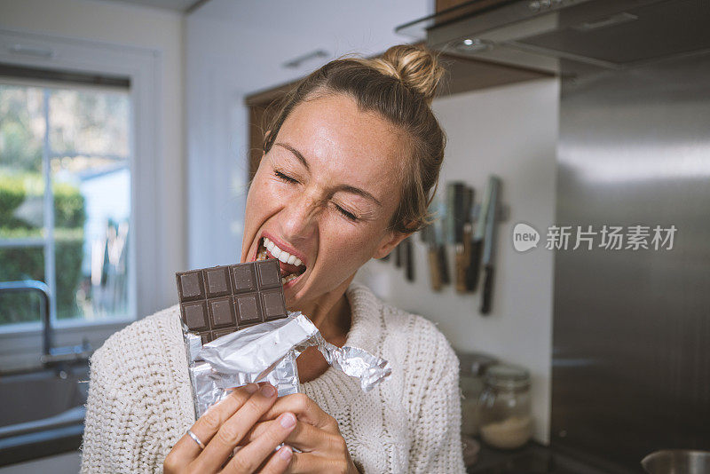 年轻女子在厨房吃巧克力，近距离观看;人们对甜食的嗜好概念