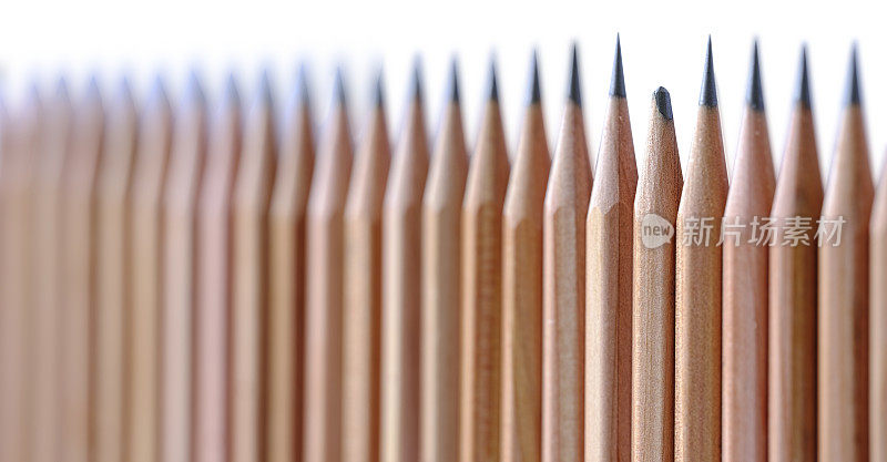 白色背景上的一排非常锋利的木铅笔，中间放着一支钝铅笔。概念形象与脱颖而出，破碎，低人一等，不同，成就不足等有关。景深浅，聚焦在钝铅笔上。