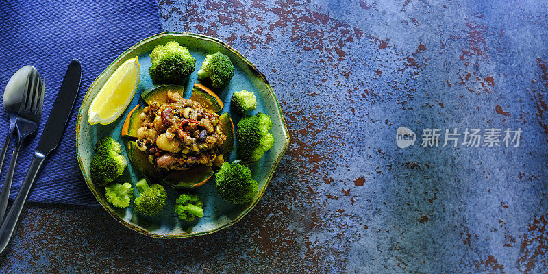 以抽象的蓝色背景为背景，用各种豆类和豆类制成的超级素食辣辣椒配以蒸熟的日本南瓜，并配以撒有柠檬汁的蒸花椰菜。