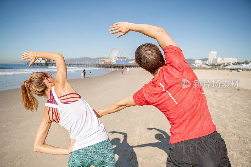 一对年轻夫妇晨跑后在海滩上伸展肌肉
