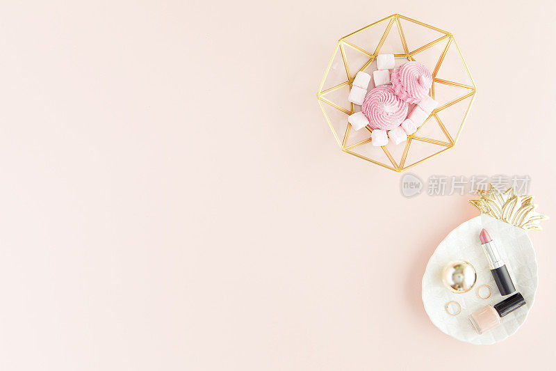 淡粉色办公桌桌子上的甜点和化妆品在现代装饰盘子。顶视图与复制空间，平放。