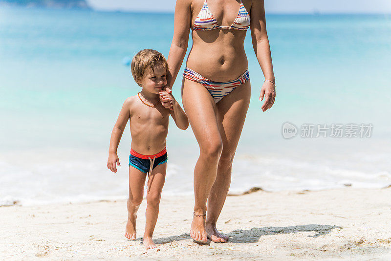 小男孩牵着不认识的妈妈走在海滩上。