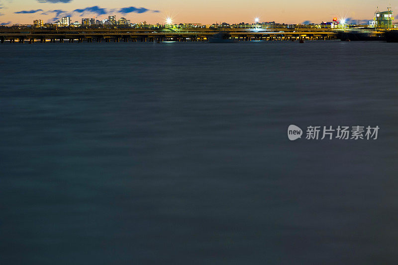 海湾夜晚有输油管道的炼油厂和城市天际线，背景有复制空间