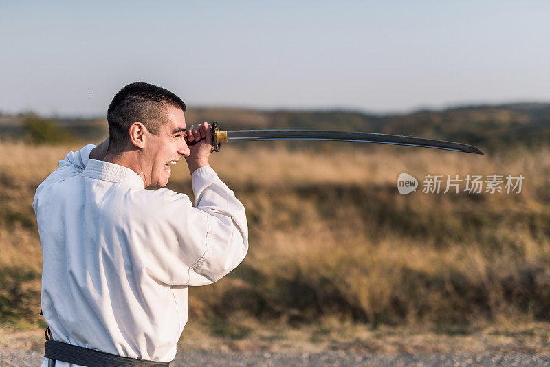 年轻的武术家用武士刀在大自然中练习技巧。