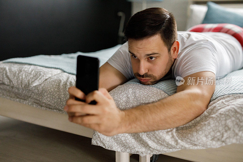 年轻人躺在卧室的床上，用智能手机
