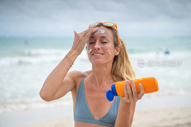 夏日――年轻女子在海滩上涂抹防晒霜，保护皮肤