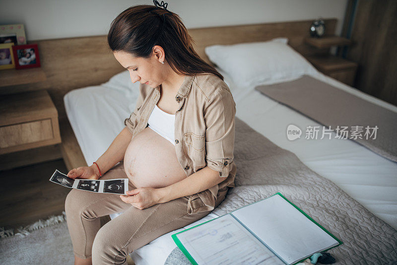 一名孕妇独自坐在卧室的床上看超声波扫描