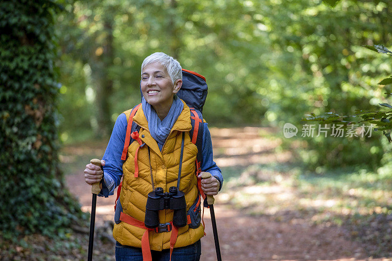 美丽成熟的老年妇女在60岁初的春天森林徒步旅行