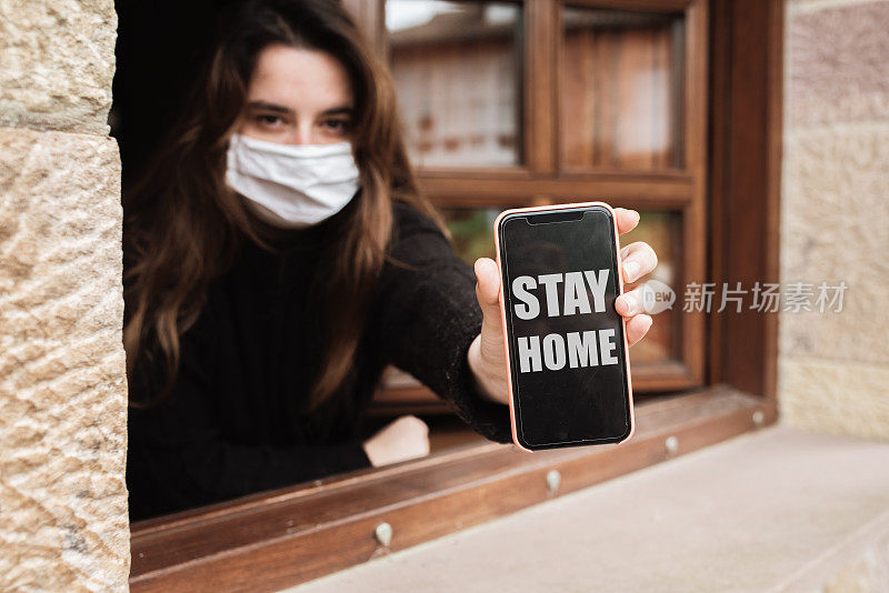 一名年轻女子在看智能手机屏幕上写着“待在家里”的建议