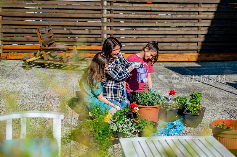 一个成年妇女和两个年轻的女孩在阳台上给新鲜的盆栽浇水