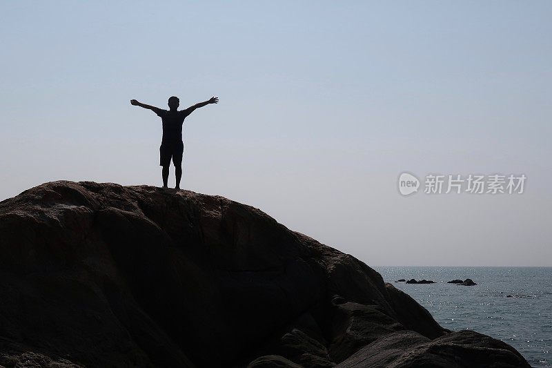 印度男游客假日站在岩石上看以橙色日落为背景的海滩，帕洛伦海滩，印度果阿