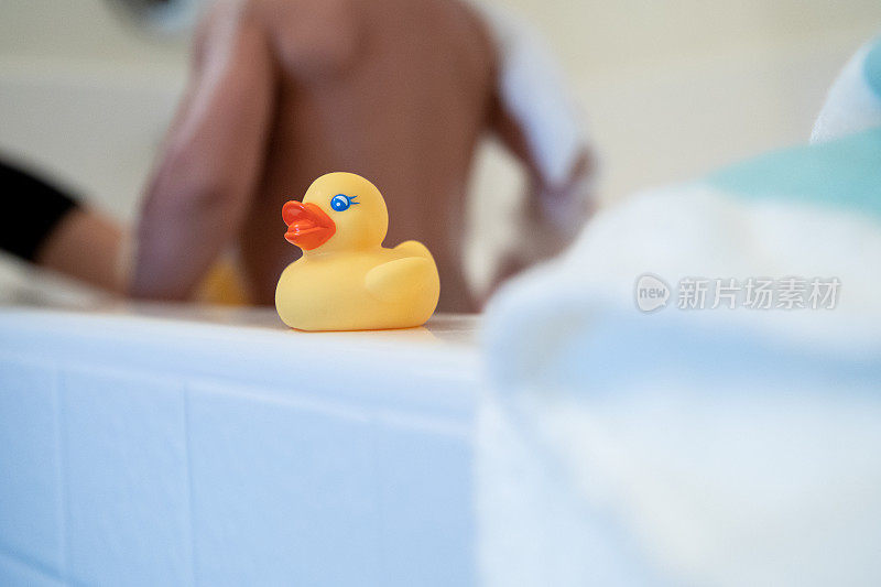 浴缸一侧的橡皮鸭玩具，母亲在背景中给孩子洗澡