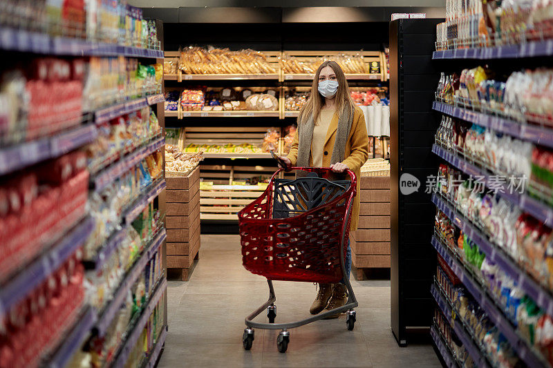 一位年轻女子戴着医用口罩推着购物车在超市里。