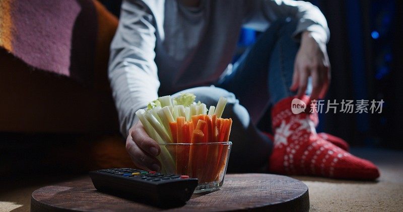 女人坐在地上，一边看电视一边吃芹菜和胡萝卜条