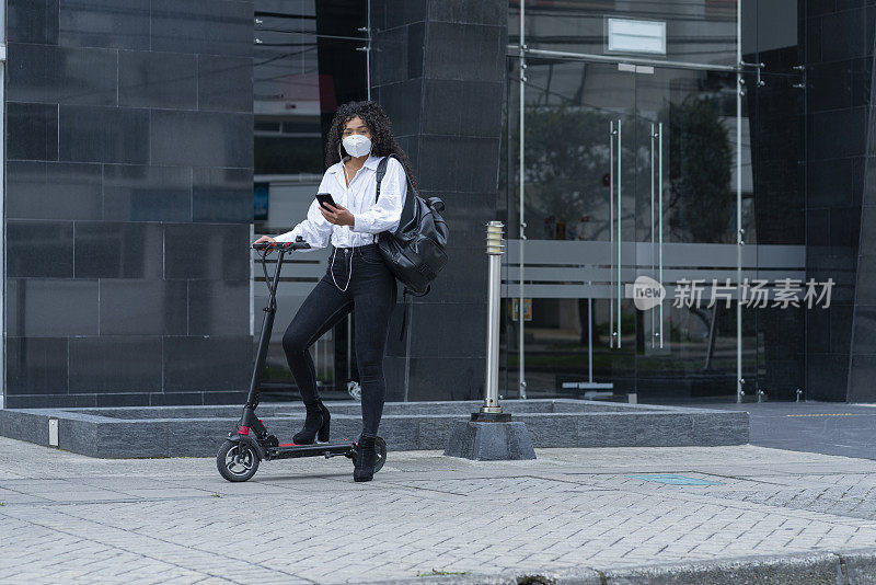 一个年轻的卷发黑发女人骑着她的电动滑板在街上听着音乐去工作的肖像