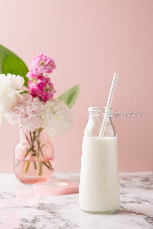 一瓶牛奶放在大理石桌上，粉红色的背景和粉红色和白色的花束，明亮和柔和的饮料组成