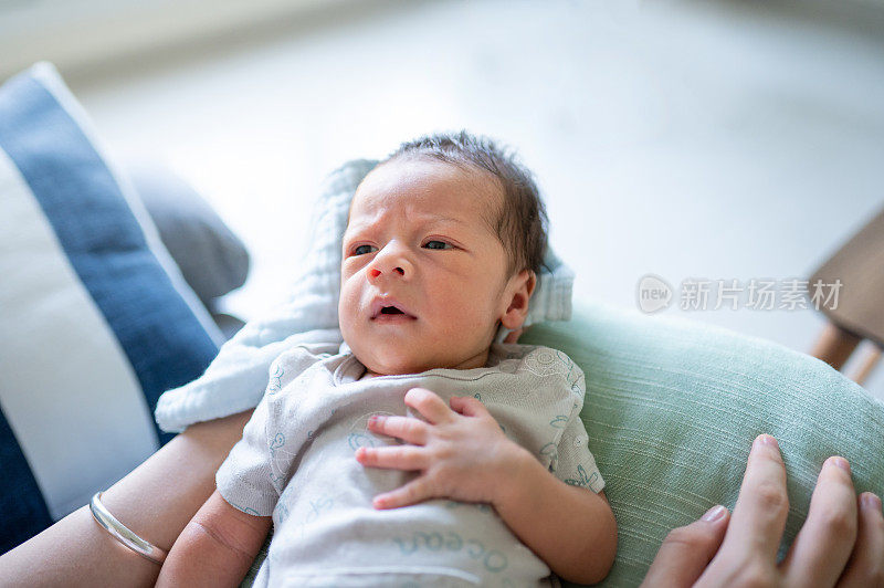一位妇女抱着刚出生两周的男婴坐在家里客厅的沙发上