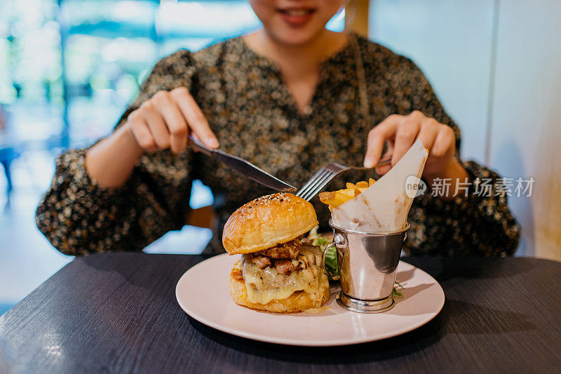 年轻的亚洲女人在咖啡馆里享用汉堡和薯条