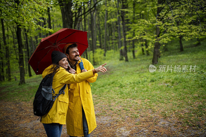 幸福可爱的情侣穿着雨衣在森林里享受雨天