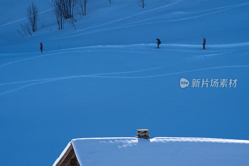 一个被雪覆盖的小屋的屋顶和三个越野滑雪者经过