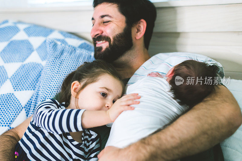 快乐的父亲享受与刚出生的婴儿和蹒跚学步的女儿在家里的优质时间