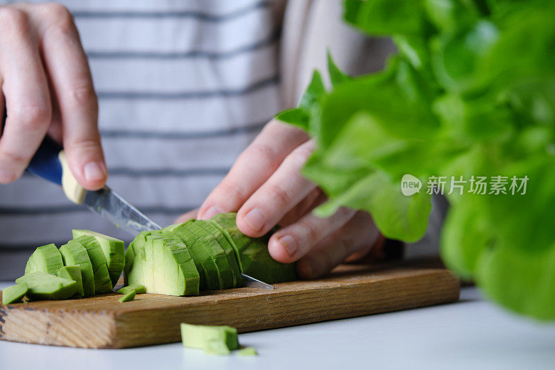 人手正在用生菜、芹菜茎、青苹果、橙子和鳄梨准备生沙拉