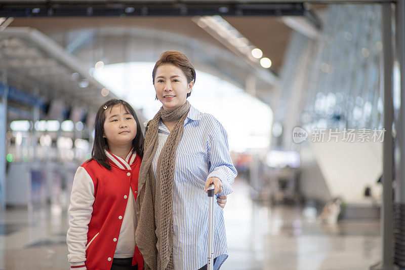 亚洲华人母女带着行李穿过机场候机楼。