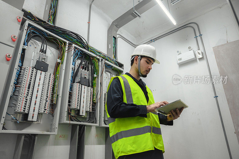 电气工程师小组工作前控制面板，电气工程师正在安装和使用平板电脑，以监测操作的一个电气控制面板在工厂服务室。