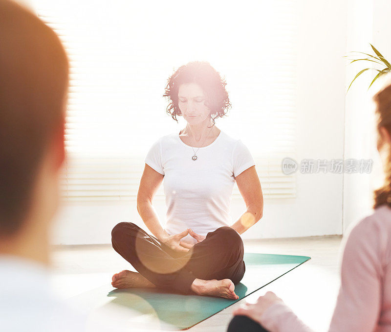 瑜伽教练在健身教室里训练人们。一位女瑜伽士在室内的一堂课上教授冥想呼吸技巧，以莲花姿势练习禅能