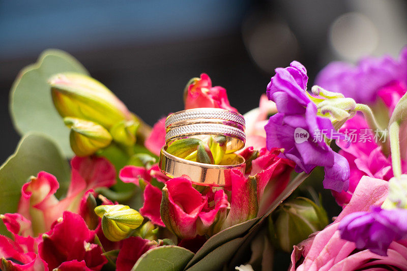 新娘和新郎的结婚金戒指躺在新娘的一束花的背景，金戒指
