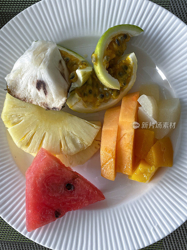 特写图像，新鲜的热带水果沙拉，菠萝切片，切碎的西瓜，木瓜，椰子，酸果和西番莲在白色盘子上，上升视图
