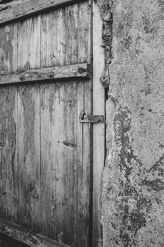 这扇旧门是黑白相间的。旧建筑的一部分是灰色的。一扇旧木门。