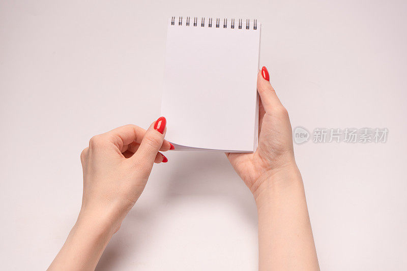一个涂着红指甲的女人手里拿着一个空白的白纸笔记本。