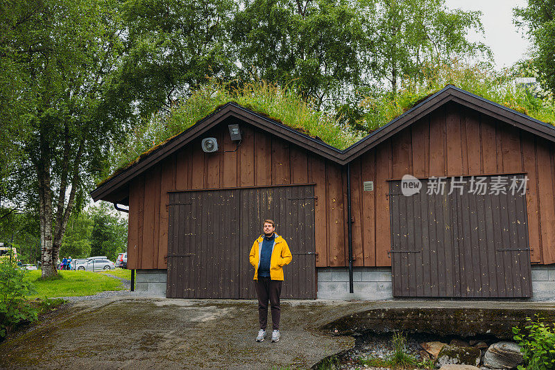 挪威，一名穿黄色夹克的男子和一只狗呆在草屋边