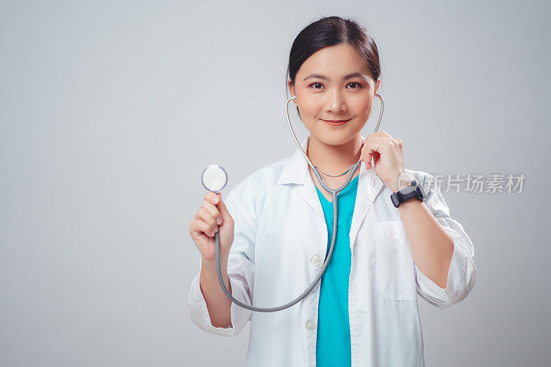 穿着医生制服的亚洲妇女医生开心地微笑着拿着听诊器孤立在白色背景。