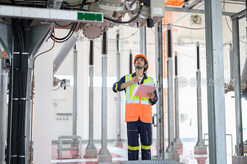 年轻的亚洲电气技术员男性工人带着个人安全设备使用图纸检查表蓝图操作或例行检查高压变电站高压断路器开关状态。