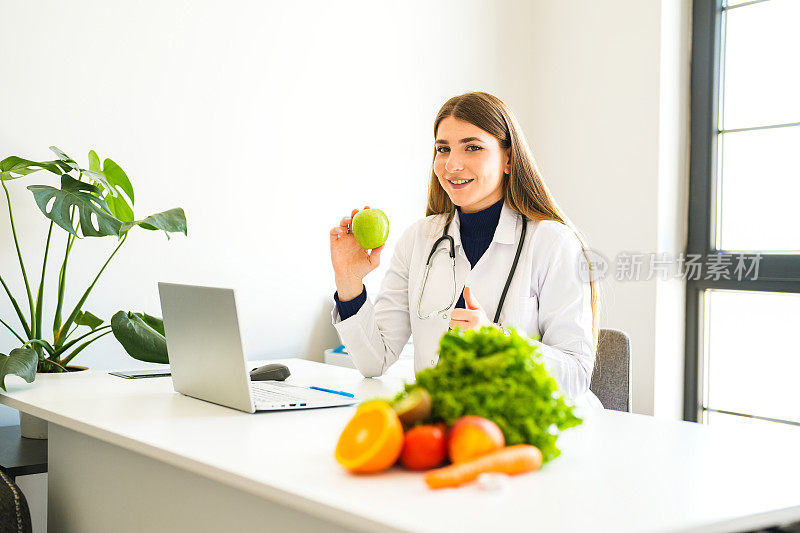 年轻漂亮的金发女郎健康营养学家在办公室里准备一份在线饮食清单，正在给她的笔记本电脑看苹果