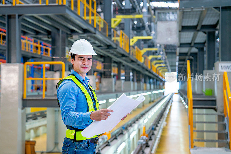 专业工程师手持施工图纸或计划，并在电气或空中列车工厂工作场所查看相机。