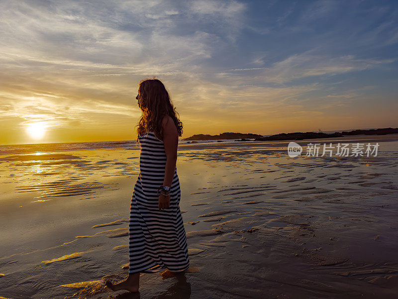 一个年轻美丽的女孩在日落时分漫步在葡萄牙的海滩上