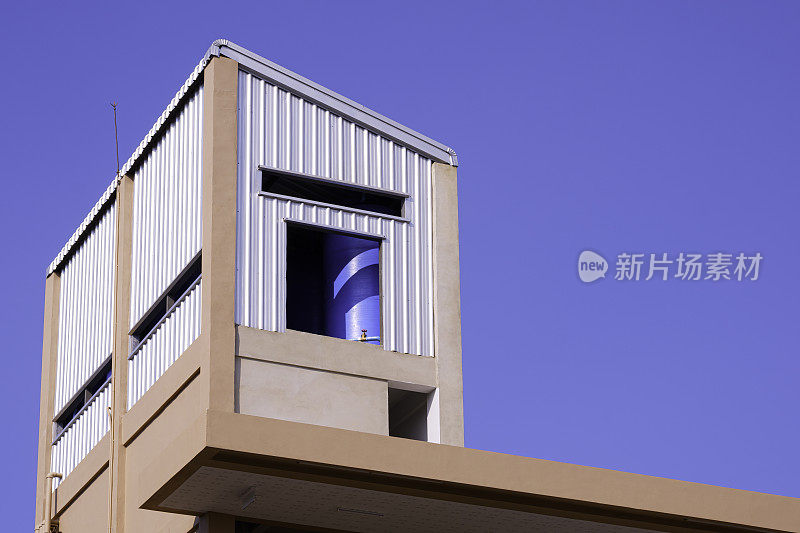 公寓屋顶波纹钢房内的大型蓝色塑料储水箱，背景是蓝色的天空
