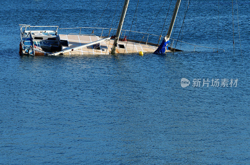 沉没的游艇-帆船斜倚在平静的蓝色水域在白天