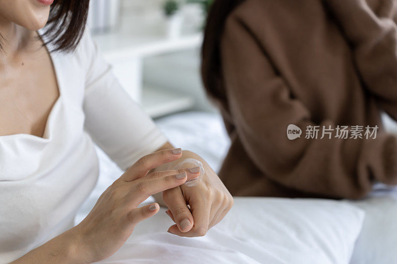 女性在床上舒舒服服地坐在床上，用手涂抹保湿霜，进行护肤治疗