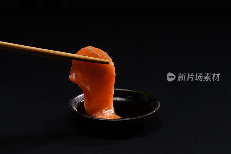 特写筷子与新鲜鲑鱼刺身蘸酱油。日式料理