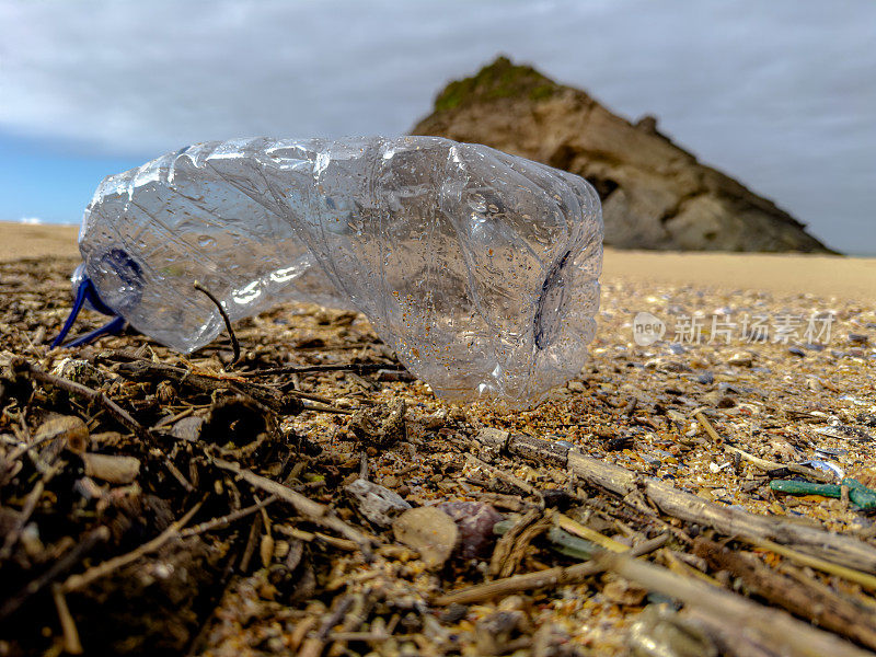 在葡萄牙的沙滩上，一个装满垃圾的空塑料瓶被疏忽地遗忘在沙滩上