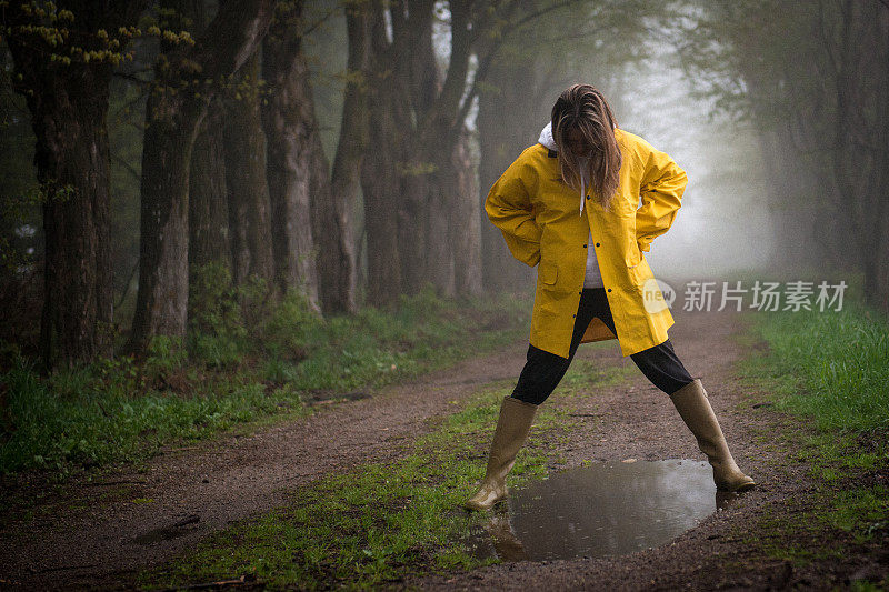 一位穿着雨衣的女性在水坑上徘徊。