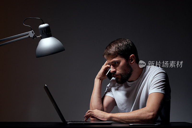 带着笔记本电脑坐在桌子旁的男人深色背景的工作场所办公室情绪灯用手手势模型裁剪视图